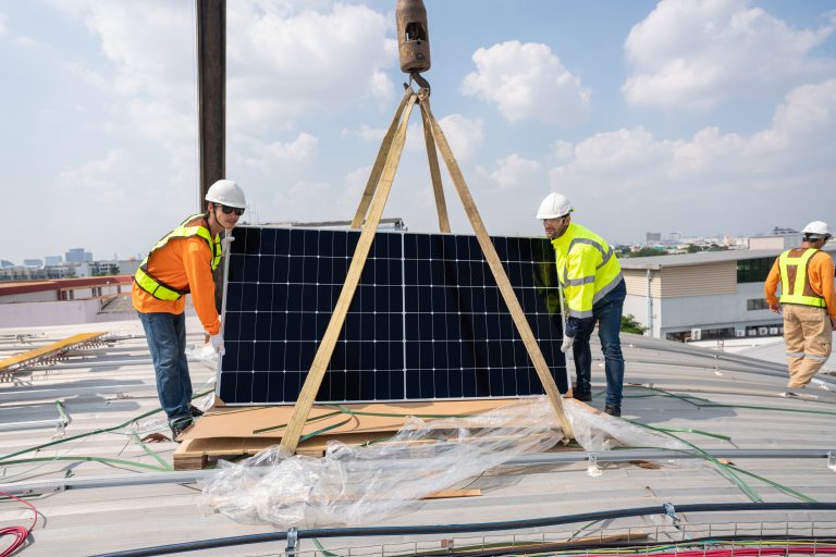 Team technicians carrying photovoltaic solar moduls on roof of factory on the morning. Installing a Solar Cell on a Roof. Solar panels on roof. Workers installing solar cell power plant eco technology.